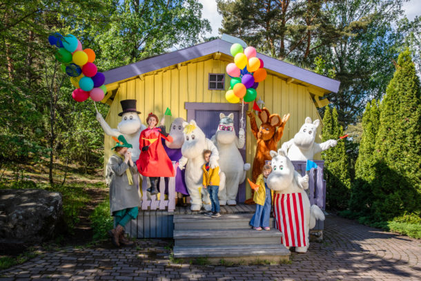 Moomin characters and kids in front of the Hemulens House.